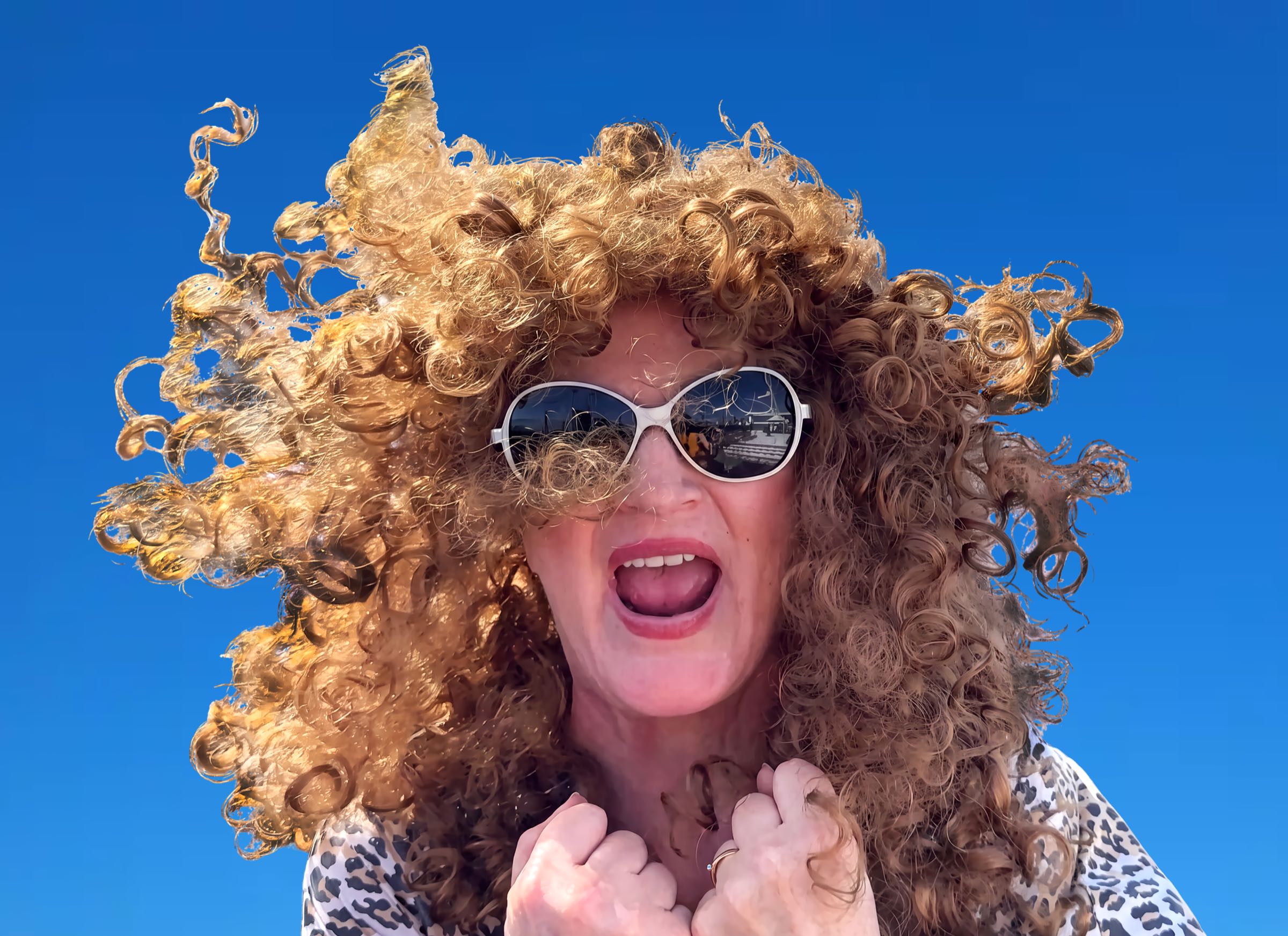 September L. Davis, hair wild, sunglasses on, mid-shout against a blue sky
